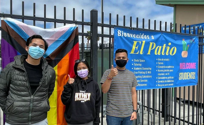 Three masked students standing and waving in front of El Patio